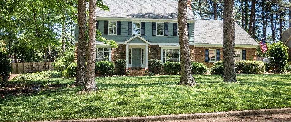 A blue and brick house in Memphis, TN, with a fertilized lawn shaded by trees.