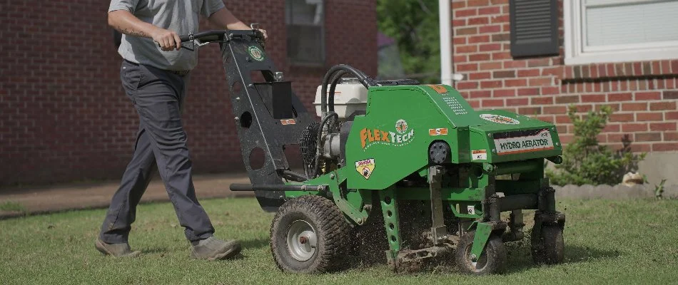 Man pushing an aerator machine across a lawn in Memphis, TN.