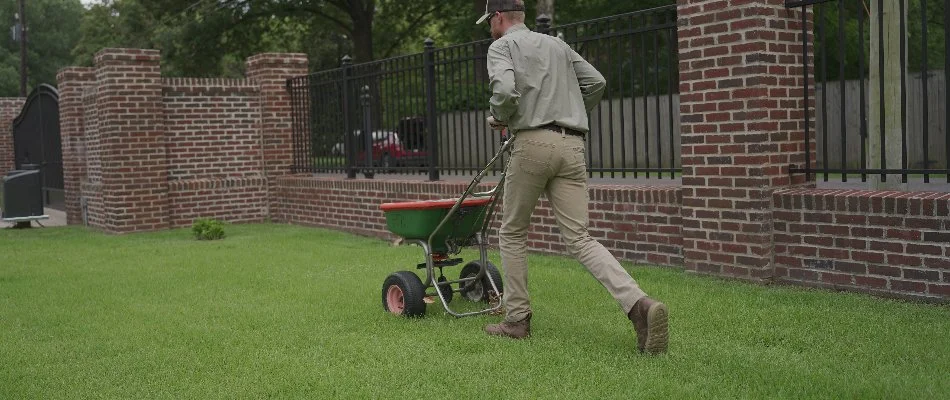 Tech pushing a granular spreader across grass in Memphis, TN.