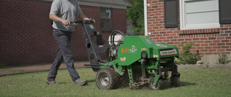 Worker pushing a core aerator across a lawn in Memphis, TN.