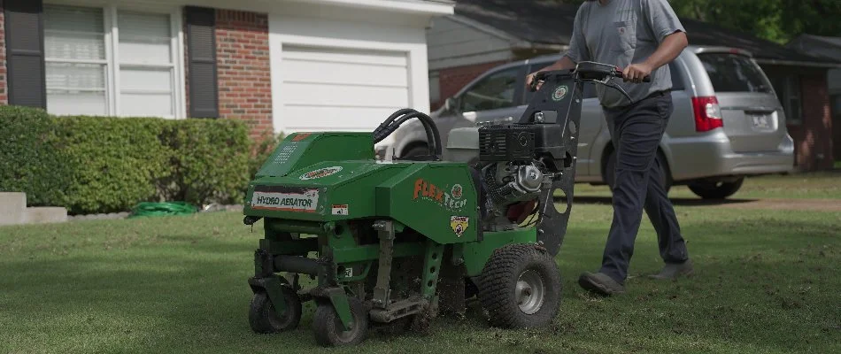 Worker pushing an aerator machine across a lawn in Memphis, TN.